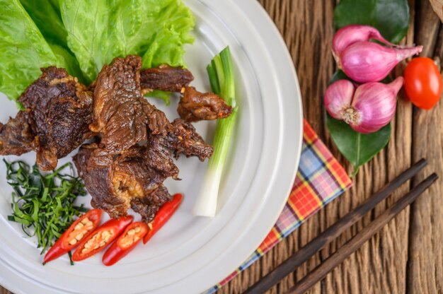 Rindfleisch gebratenes thailändisches Essen auf einem weißen Teller mit Frühlingszwiebeln, Kaffirlimettenblättern, Chilis, Salat, roten Zwiebeln und Tomaten.