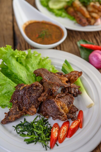 Rindfleisch gebratenes thailändisches Essen auf einem weißen Teller mit Frühlingszwiebeln, Kaffirlimettenblättern, Chilis, Salat und Chilipaste in einer Tasse.