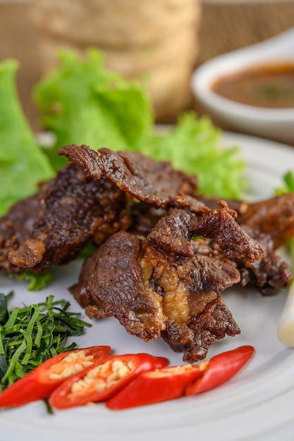 Rindfleisch gebratenes thailändisches Essen auf einem weißen Teller mit Frühlingszwiebeln, Kaffirlimettenblättern, Chilis, Salat und Chilipaste in einer Tasse.