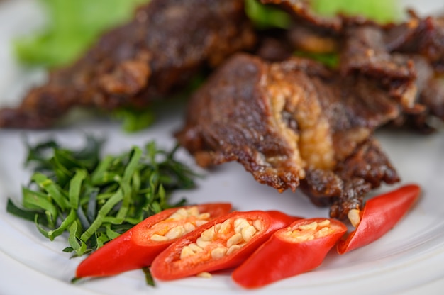 Rindfleisch gebratenes thailändisches Essen auf einem weißen Teller mit Frühlingszwiebeln, Kaffirlimettenblättern, Chilis, Salat und Chilipaste in einer Tasse.