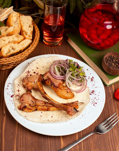 Rindfleisch, Lammkarreekebab diente mit Zwiebelscheiben, Gemüse und Kräutern, Lavash in der weißen Platte.