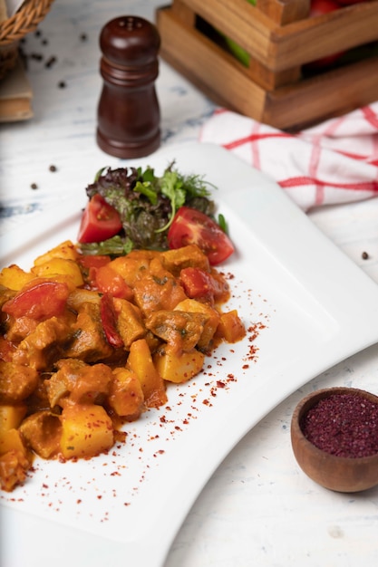 Kostenloses Foto rindfleischscheiben eintopf in tomatensauce mit zwiebeln und paprika. serviert in weißen teller mit basilikum, schwarzer pfeffer