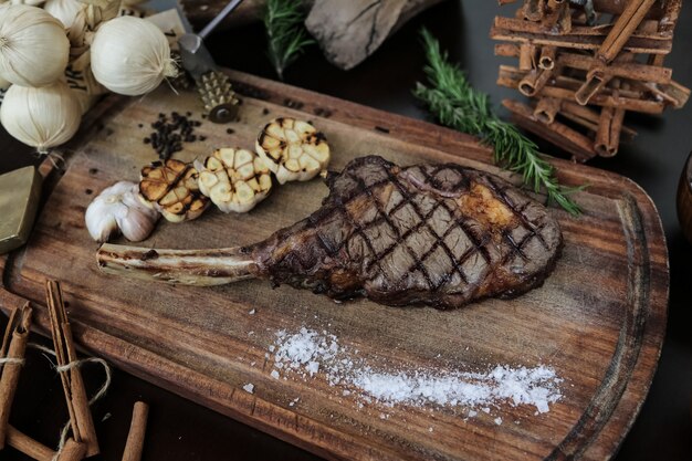 Rippensteak von oben mit gegrilltem Knoblauch und Salz auf einem Ständer mit Rosmarin und Zimt