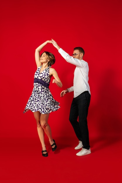 Rock 'n' Roll. Altmodische junge Frau, die lokalisiert auf rotem Studiohintergrund tanzt. Junger stilvoller Mann und Frau.