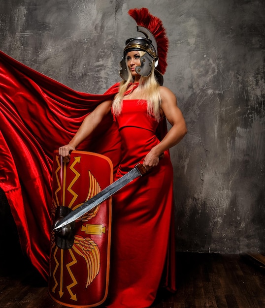 Kostenloses Foto römische kriegerin im roten flatternden kleid hält schwert und schild.