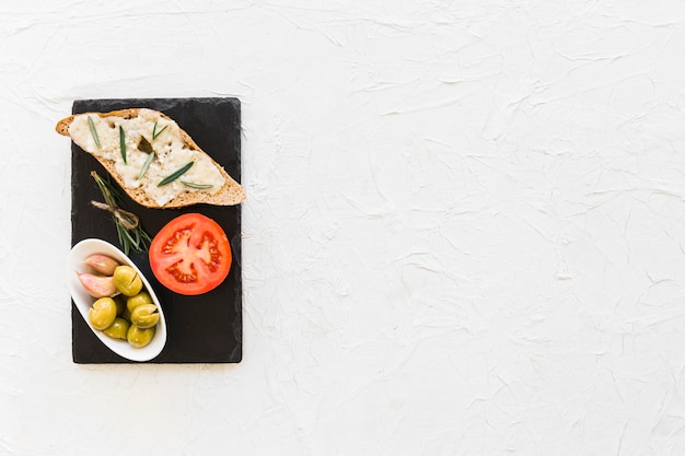 Rösten Sie Brot mit Käse-, Rosmarin-, Tomaten- und Olivenschüssel auf Schieferplatte