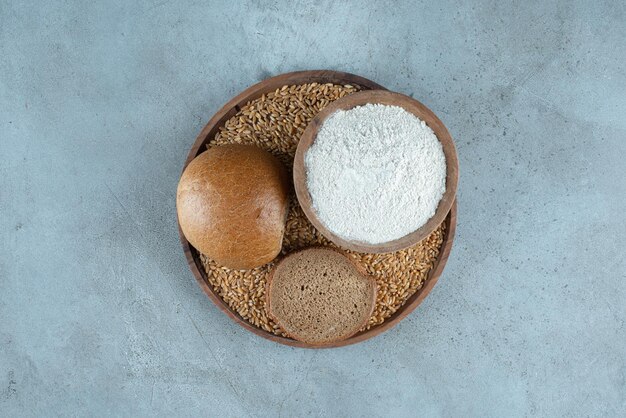 Roggenbrötchen mit Schüssel Mehl auf Holzplatte.