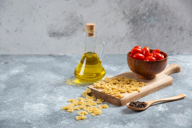 Rohe Farfalle, Tomaten und Olivenöl auf Holzbrett.