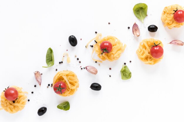Rohe Fettuccineteigwaren; Kirschtomate; schwarze Olive; Knoblauchzehen- und Basilikumblätter lokalisiert über weißem Hintergrund