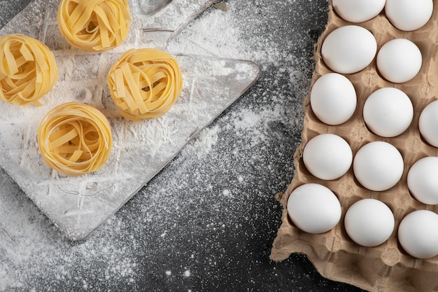 Rohe frische Tagliatelle-Nester mit Mehl auf Holzbrett und Eiern