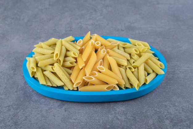 Rohe grüne und gelbe Penne-Nudeln auf blauem Teller.