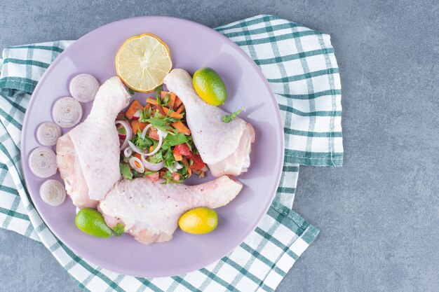 Rohe Hähnchenschenkel mit Gemüse auf lila Platte.