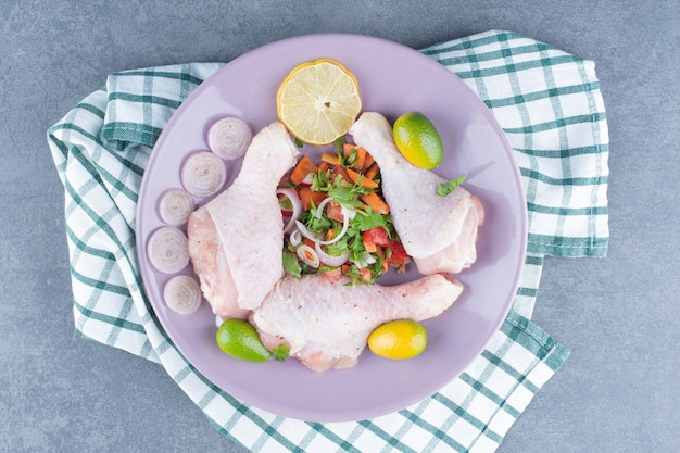 Rohe Hähnchenschenkel mit Gemüse auf lila Platte.