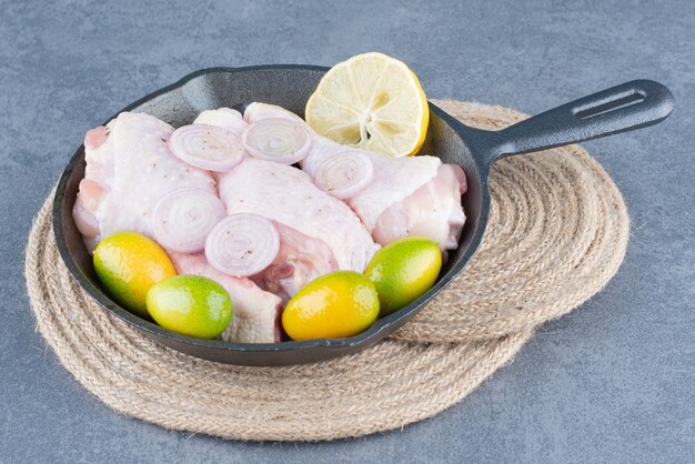 Rohe Hähnchenschenkel mit Gemüse in schwarzer Pfanne.