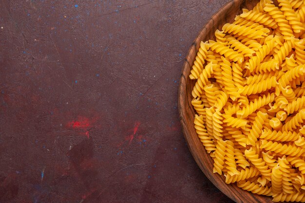Rohe italienische Nudeln der Draufsicht innerhalb des Holztabletts auf dunklem Hintergrundproduktnudelmahlzeit-Lebensmittelgemüse
