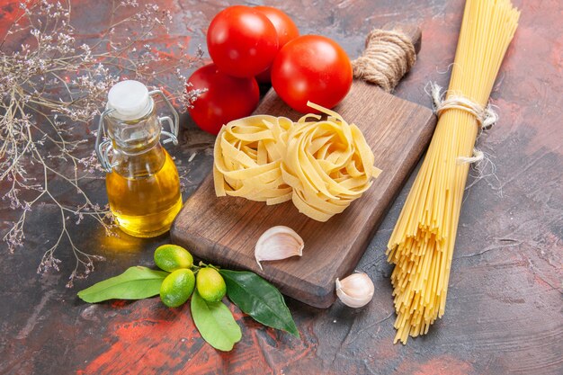 Rohe Nudeln der Vorderansicht mit Öltomaten und Knoblauch auf rohem Nudelteig der dunklen Oberfläche