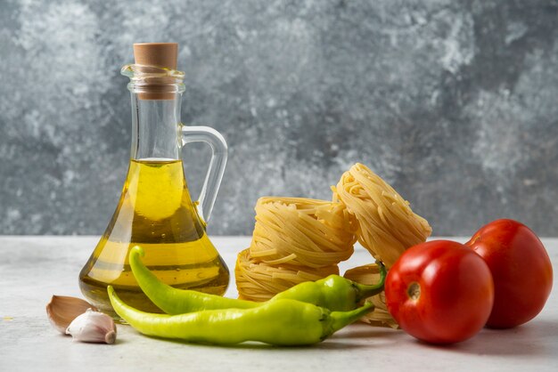 Rohe Nudelnester, Flasche Olivenöl und Gemüse auf weißem Tisch.