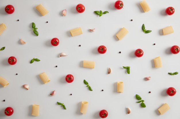 Rohe Rigatoni-Nudeln aus Hartweizenmehl, roten reifen Tomaten und grünem Basilikum auf weißem Hintergrund. Zutaten für die italienische Küche. Traditionelle Küche. Nourishig Nudelgericht und Lebensmittelkonzept