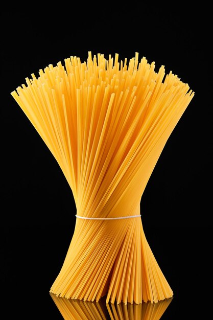 Rohe Spaghetti, die in einer Garbe gebunden sind, stehen auf einem dunklen Glas auf schwarzem Hintergrund italienische Vollkorn-Spaghetti-Nudeln