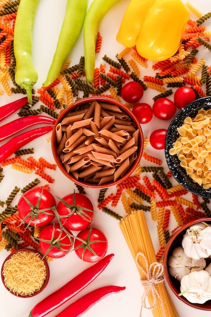 rohe Spaghetti mit Tomaten, grünem Chili und rotem Chili auf einer weißen Oberfläche