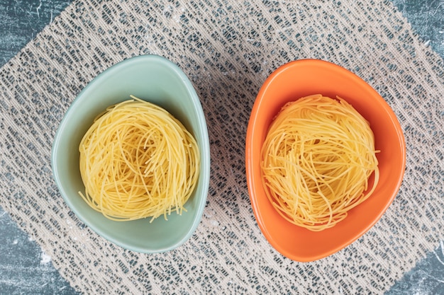 Kostenloses Foto rohe spaghetti-nester in bunten schalen und sackleinen. hochwertiges foto