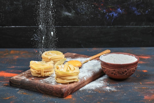 Rohe Tagliatelle-Nudeln auf Holzbrett mit Schüssel Pulver.