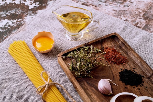 Rohe trockene Spaghetti und getrocknete Kräuter und Eier auf brauner Tischdecke.