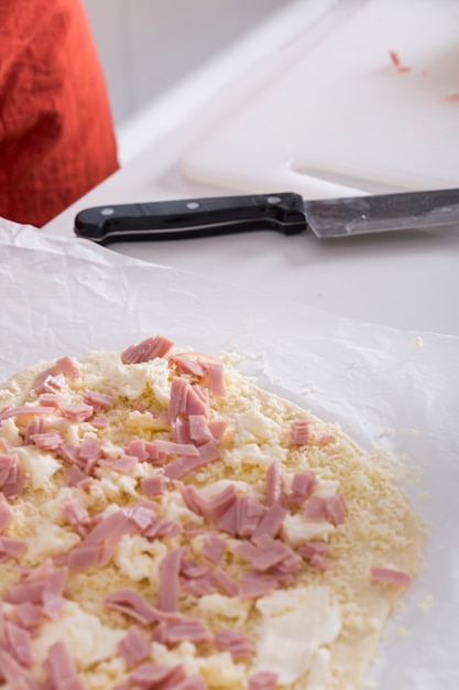 Kostenloses Foto roher pizzateig mit bestandteilen auf weißem pergamentpapier