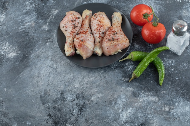 Roher würziger Hühnertrommelstock mit Tomate und Pfeffer auf grauem Hintergrund.