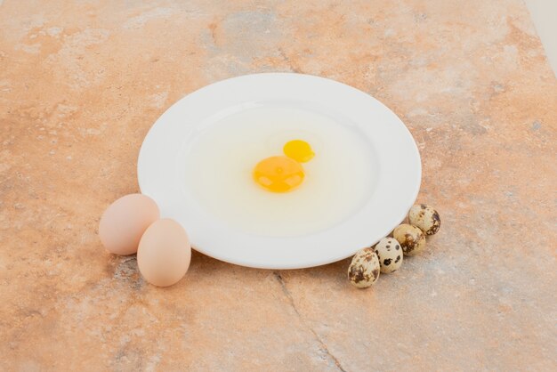 Rohes Ei auf weißem Teller und mehrere Wachteleier.