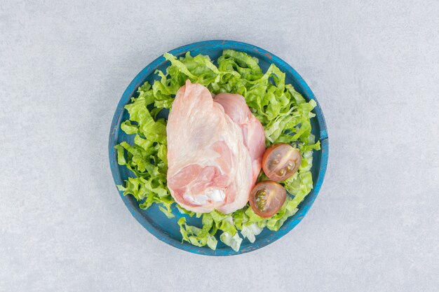 Rohes Fleisch, Tomaten und Gemüse auf dem Teller auf der Marmoroberfläche