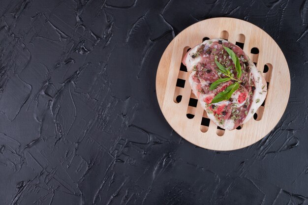 Rohes Fleischstück auf Holzteller verziert mit frischer Minze auf dunklem Hintergrund.