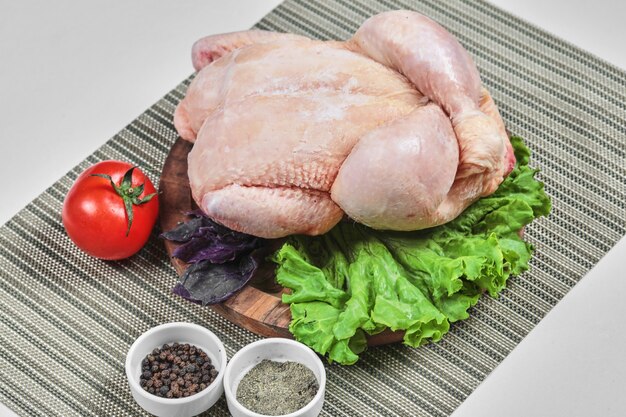 Rohes ganzes Huhn auf Holzteller mit Salat, Tomate und Gewürzen