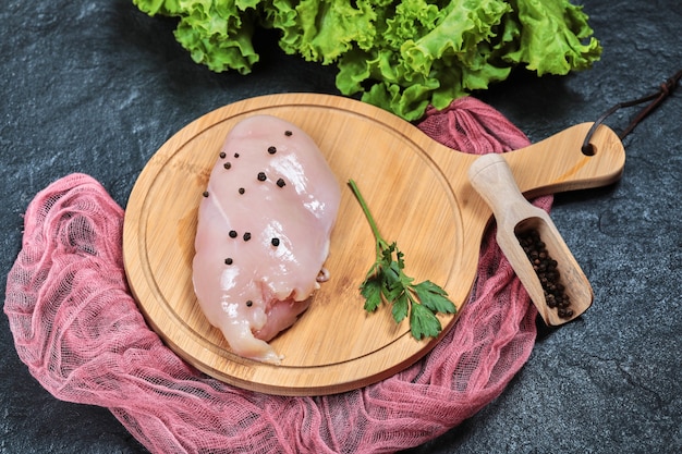 Kostenloses Foto rohes hähnchenfilet auf holzbrett mit gemüse und tischdecke.