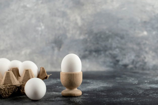 Rohes Hühnerei in Eierbecher mit Eierkasten auf einer Marmoroberfläche.