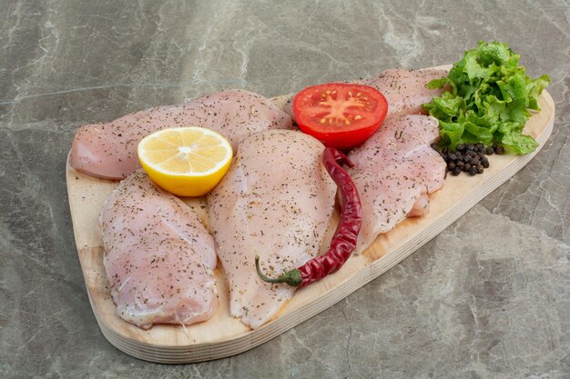 Rohes Hühnerfleisch mit Pfeffer, Tomate und Zitrone auf Holzbrett. Foto in hoher Qualität