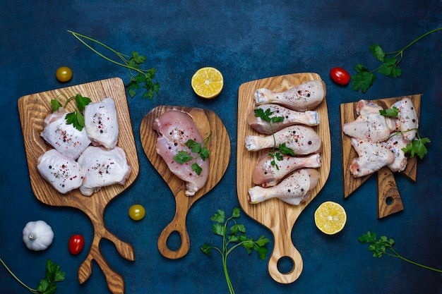 Rohes Hühnerfleischfilet, -schenkel, -flügel und -beine mit Kräutern, Gewürzen, Zitrone und Knoblauch auf dunkelblauem Hintergrund. Ansicht von oben