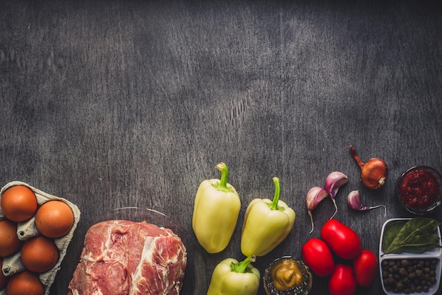 Rohes Schweinefleisch auf dunkler Holzoberfläche und Zutaten zum Kochen. Lebensmittelhintergrund mit Kopienraum. Stillleben. Flach liegen