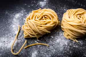 Kostenloses Foto rohes selbst gemachtes capellini-teigwarennest mit mehl auf einem schwarzen hintergrund