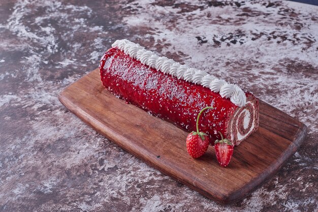 Rollen Sie Kuchen mit roter Marmelade auf einem Holzbrett mit Beeren herum.