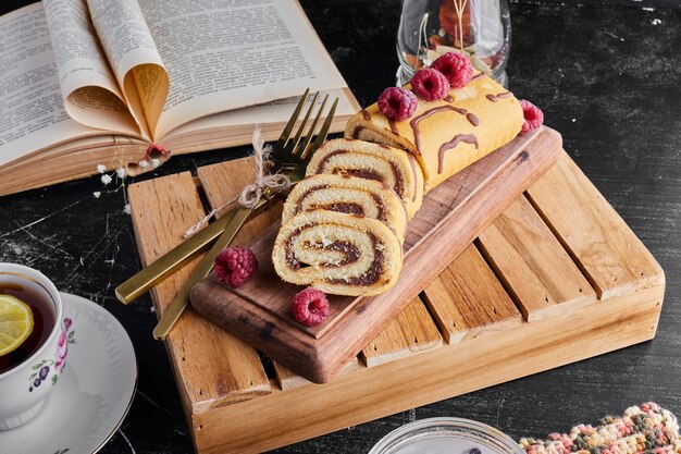 Rollen Sie Kuchen mit Schokoladencreme und einer Tasse Tee auf einem Holztablett.