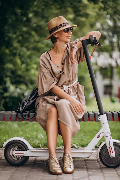 Kostenloses Foto roller der jungen frau reitim park, der auf bank sitzt