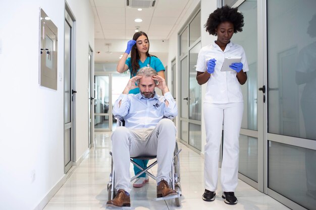 Rollstuhlpatient mit professioneller afroamerikanischer Ärztin und Krankenschwester Fachpersonal im Korridor des Krankenhaus-Erholungszentrums