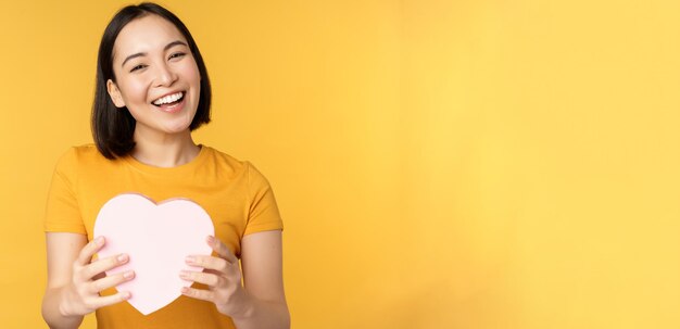 Romantik und Valentinstag glückliche schöne asiatische Frau, die eine große Herzkarte hält und stehend o lächelt