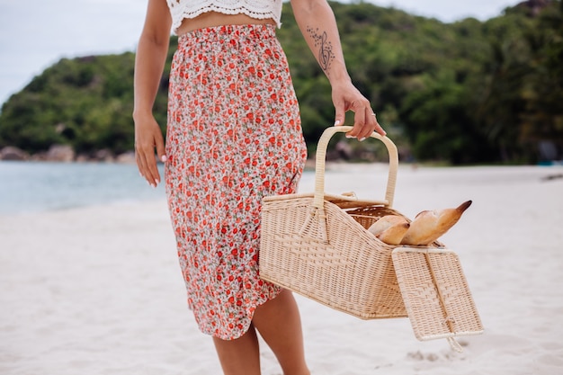 Romantische Frau am Strand im Rock gestricktes Oberteil und Strohhut, die Korb mit Brot Eco Leben halten