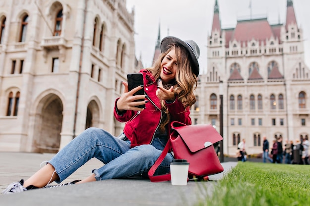 Romantische Frau in Retro-Jeans, die auf dem Boden sitzt und Videoanruf für Gespräch verwendet