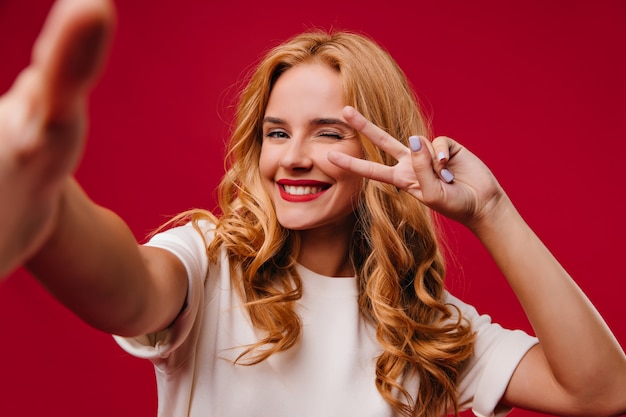 Romantische junge Frau mit trendiger Maniküre, die auf roter Wand aufwirft. Entzückende blonde Frau lacht