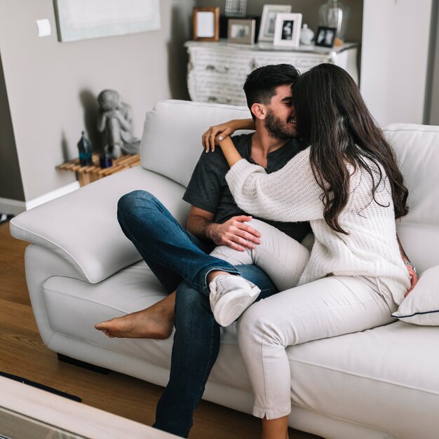 Romantische junge Paare, die auf dem weißen Sofa sich liebt sich sitzen