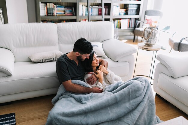 Romantische junge Paare, die zu Hause nahe Sofa in der Decke sitzen