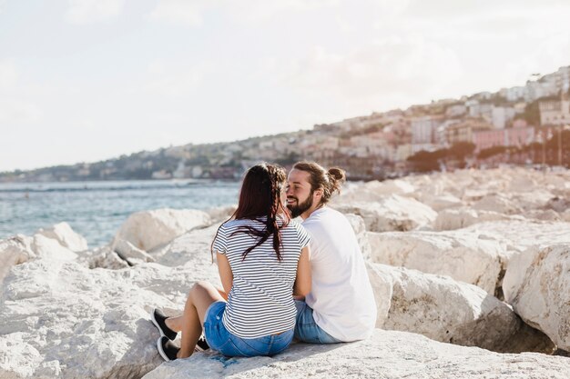 Romantische Paare, die auf Felsen in dem Meer sitzen